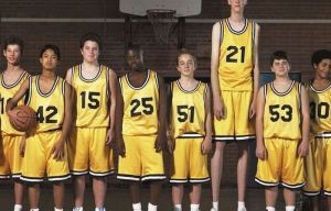 Several regular kids in basketball uniforms and one really tall kid